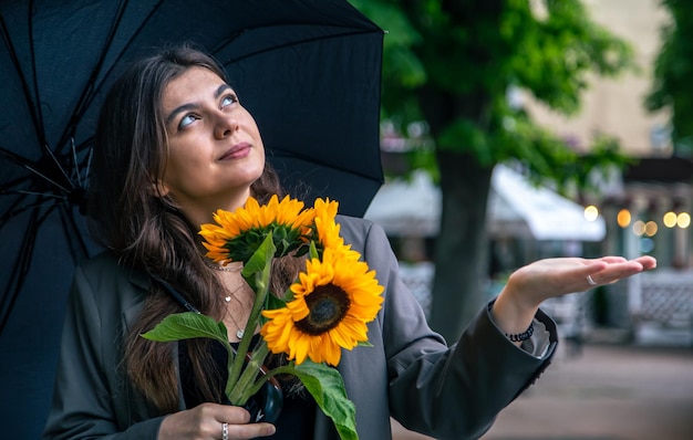 A young woman with a bouquet of sunflowers under an umbrella in rainy weather