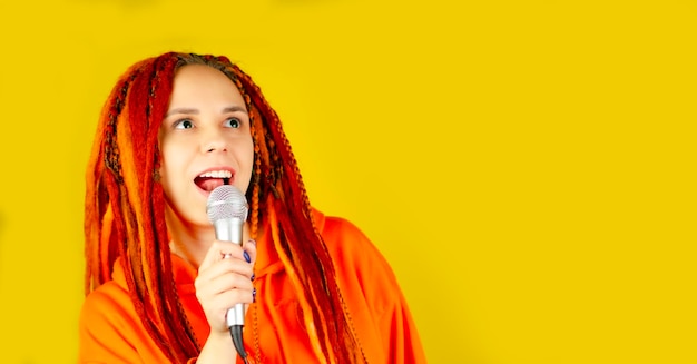 Young woman with bright dreadlocks singing into microphone on yellow background Emotional female singer with mic in studio Close up