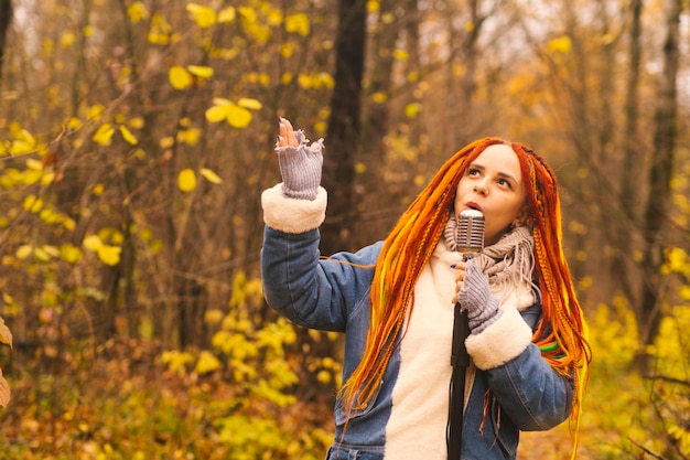 Young woman with bright hairstyle with retro microphone in autumn forest Portrait of female singer with dreadlocks singing into microphone in nature