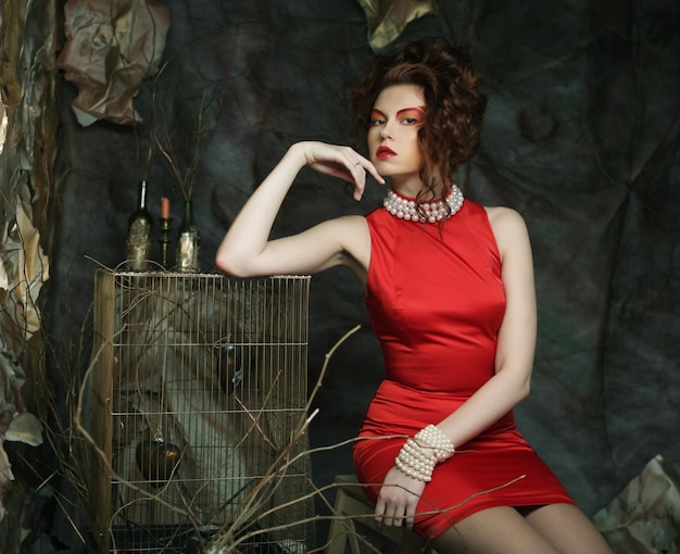 Young woman with bright makeup wearing red dress on a background of theatrical scenery