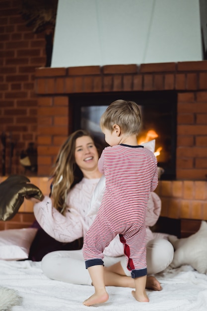 Young woman with a child. Mom and son are fooling around, having fun near the fireplace.