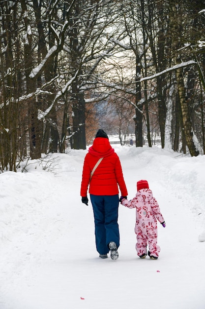 A young woman with a child walks along the snowcovered alley of the city park