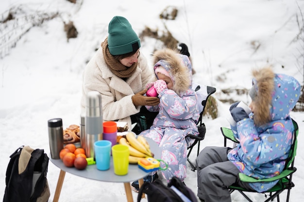 Young woman with children in winter forest on a picnic Mother and two daughters