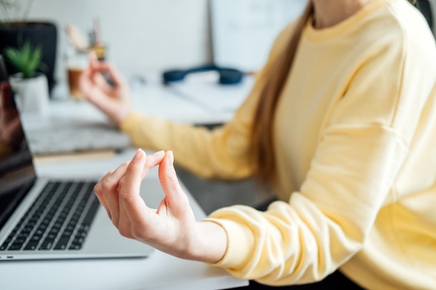 Young woman with close eyes near laptop at home office practicing meditation at table freelancer