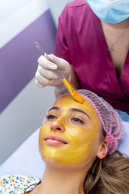 Young woman with closed eyes and golden mask on face lying on couch in beauty clinic, spa procedure.