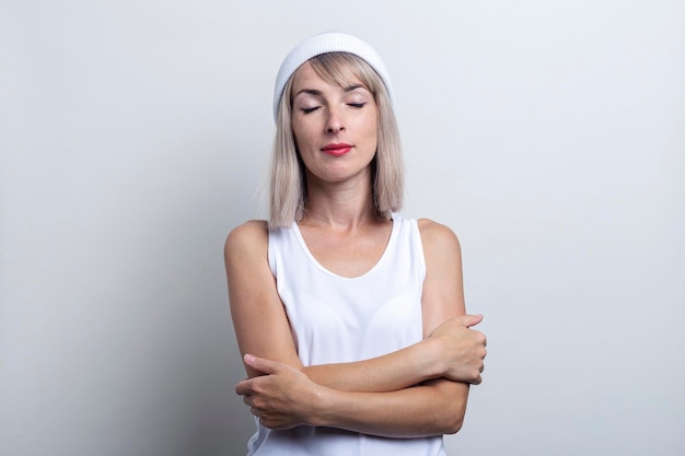 Young woman with closed eyes holds her arms crossed on a light background.