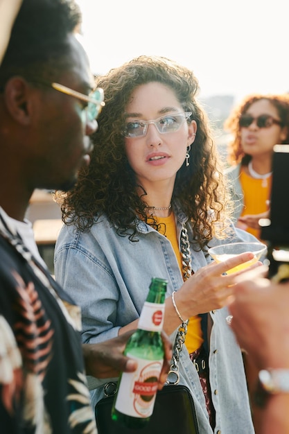 Young woman with cocktail looking at african american man with bottle of beer