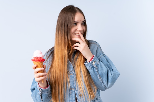 Young woman with a cornet ice cream on blue wall thinking an idea and looking side