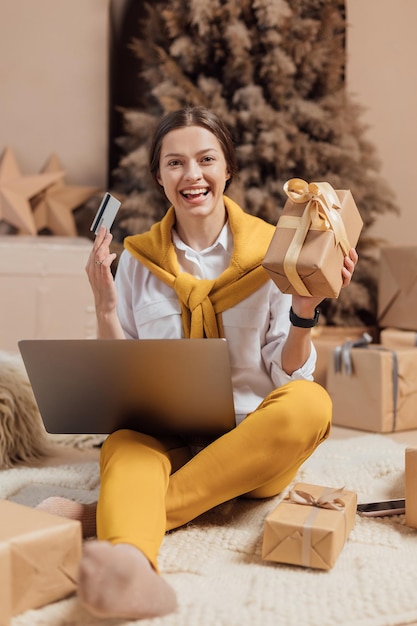 Young woman with credit card shopping online on laptop in cozy christmas interior