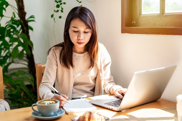 Young woman with cup of coffee sitting and working on laptop at coffee shop