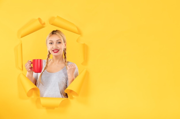 Young woman with cup of tea on a torn yellow paper background facial advertising shopping