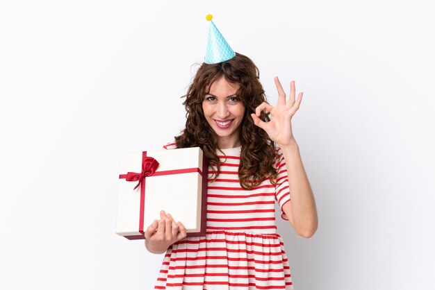 Young woman with curly hair holding present isolated on white background showing ok sign with fingers