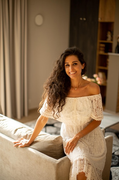 A young woman with curly hair is relaxing in the comfort of her own room dressed in a white flowing dress