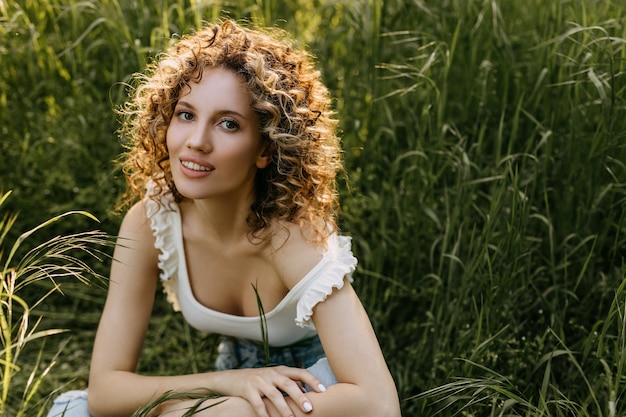 Young woman with curly hair smiling in a field with green grass