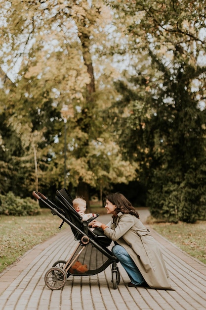 Young woman with cute baby girl in baby stroller at the autumn park