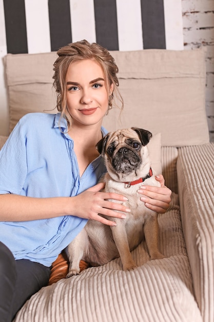 Young woman with cute pug dog on sofa at home.