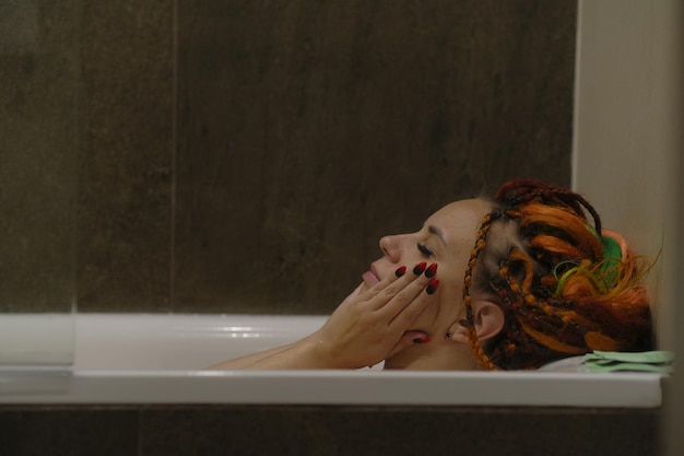 Young woman with dreadlocks bathing in bathroom Relaxed female enjoying water treatments