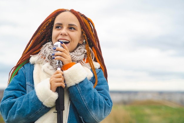 Young woman with dreadlocks singing into microphone in countryside Female singer enjoying singing in nature