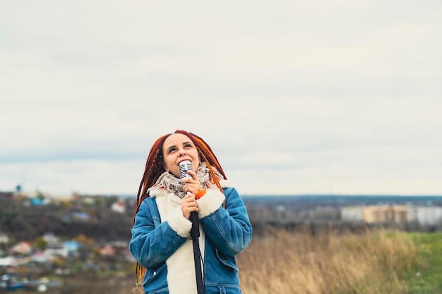 Young woman with dreadlocks singing into microphone in countryside Female singer enjoying singing in nature