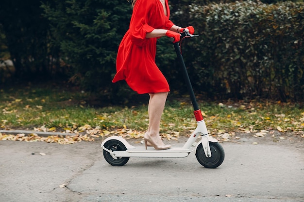 Young woman with electric scooter in red dress at the autumn city park