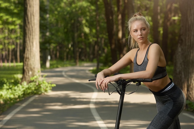 A young woman with an electric scooter in sportswear in the park