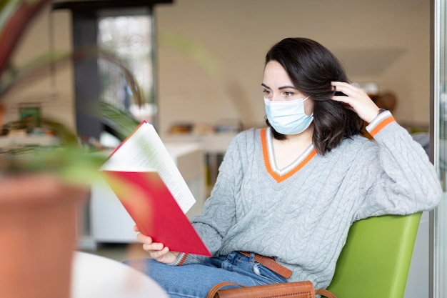 Young woman with face mask reading a book in public space Space for text