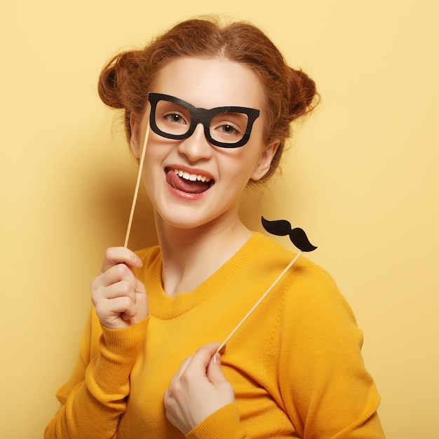 Young woman with fake mustaches and glasses over yellow backgro