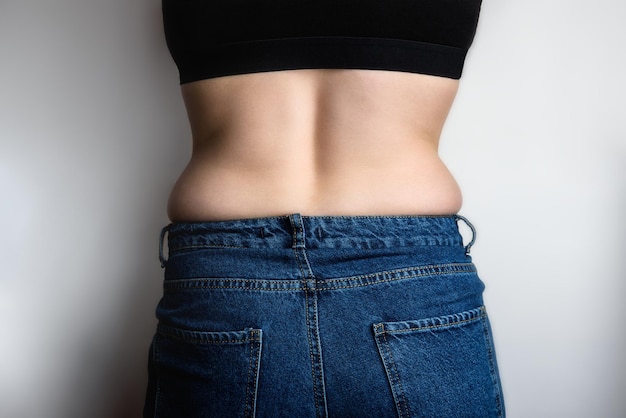 Young woman with fat folds on sides on gray background Overweight concept View from the back