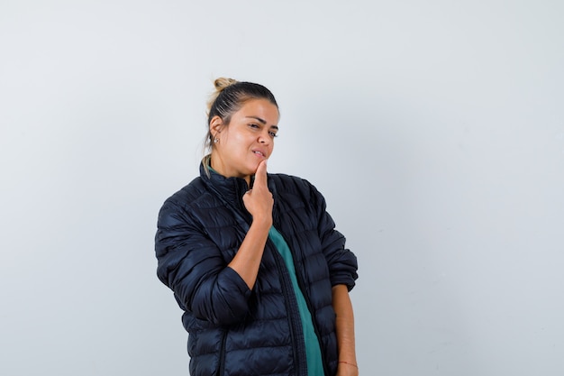 Young woman with fingers on chin in puffer jacket and looking confident , front view.