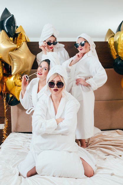 Young woman with folded arms. Incredulity and doubt. Friends behind. Girls bathrobe party. Balloons decor.