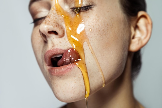 Young woman with freckles and honey on face tongue out and licking with closed eyes and passion