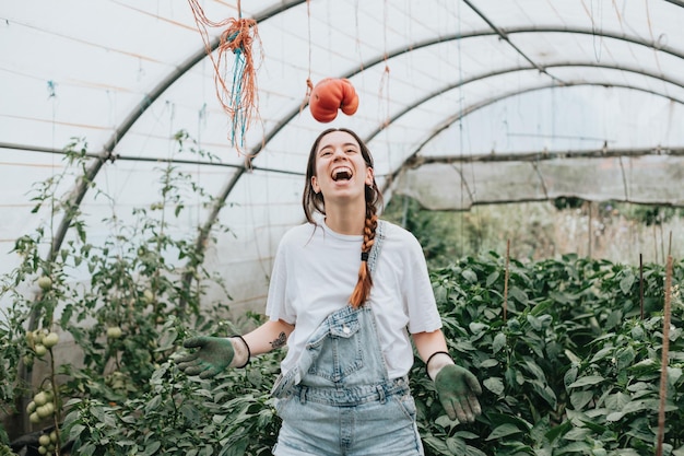 Young woman with fresh pepper at the greenhouse eating and playing with them showing the fresh vegetable to camera Rural working and resources concept hard working young woman