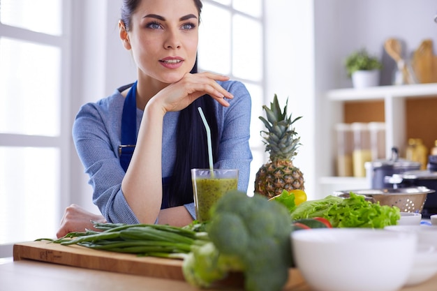 Young woman with glass of tasty healthy smoothie at table in kitchen