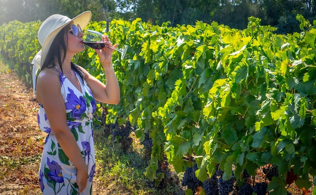 Young woman with glass of wine in vineyard on sunny day front view