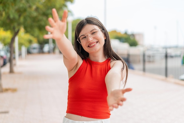 Young woman with glasses at outdoors presenting and inviting to come with hand