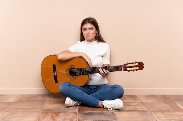 Young woman with guitar sitting on the floor sad