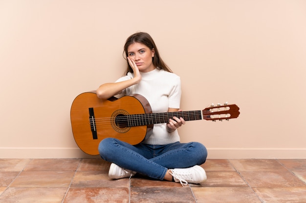 Young woman with guitar sitting on the floor unhappy and frustrated