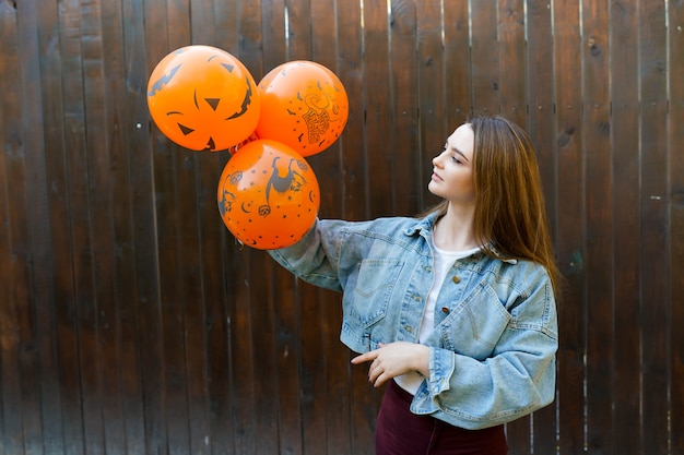 Young woman with halloween inflatable orange ballons on brown background