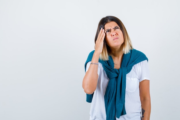 Young woman with hand on temples in white t-shirt and looking painful , front view.