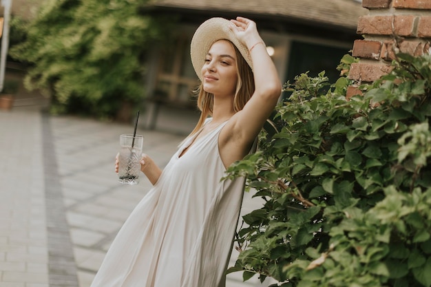 Young woman with hat drinking cold lemonade in the resort garden