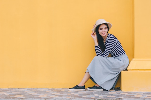 Young woman with hat,sitting next to the building.