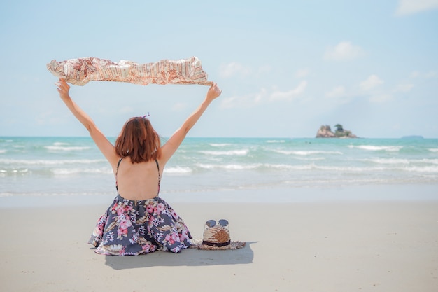 A young woman with hat and sunglasses sitting on beach