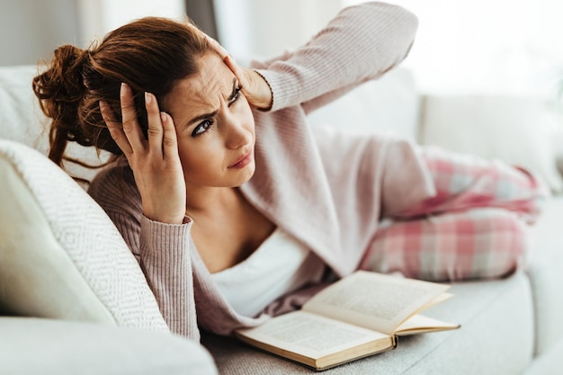 Young woman with headache holding her head in pain while lying down on sofa at home