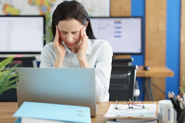 Young woman with headache behind laptop at workplace