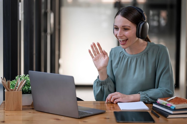 Young woman with headphone doing video call via laptop computer while sitting office