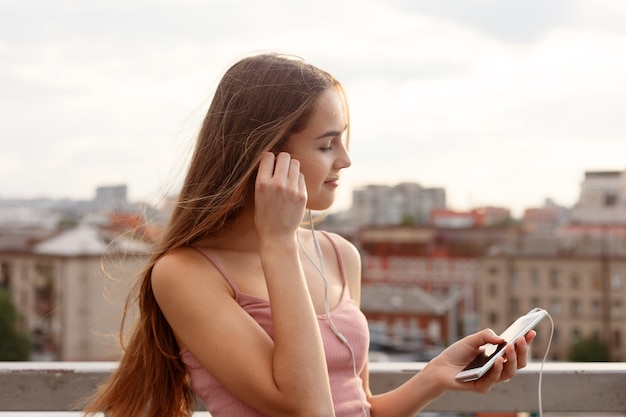 Young woman with headphones dangling on her mobile phone as she walks in an urban street