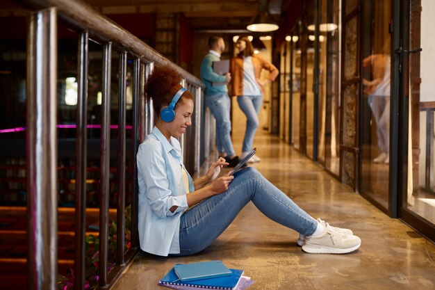 Young woman with headphones sitting on floor and using digital tablet in coworking office