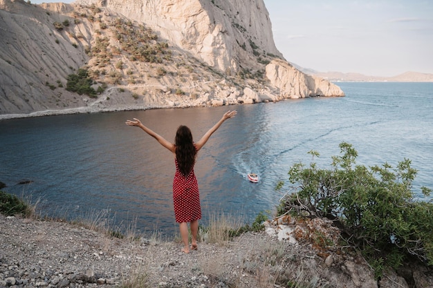 A young woman with her hands up in the fresh air against the background of the sea Place for your text