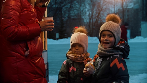 A young woman with her happy children drinking hot drinks and eating donuts