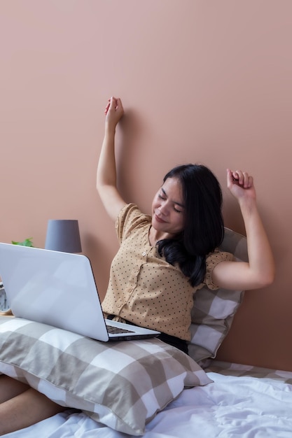 Young woman with laptop on bed while stretching hands